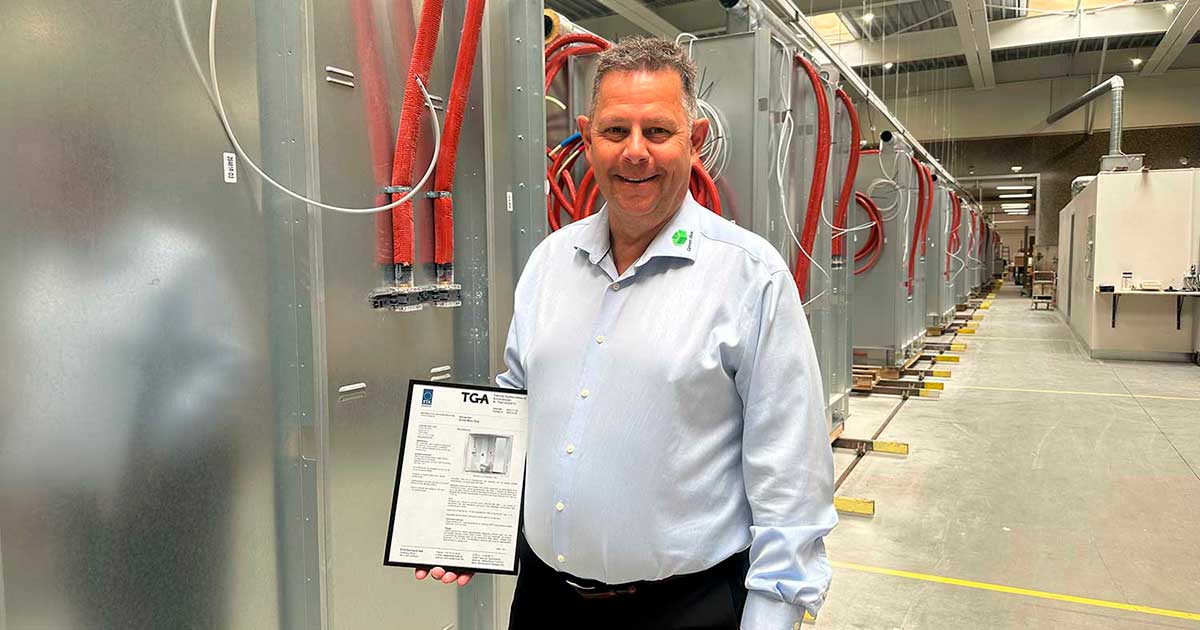 Peer Leth, CEO at Green Box A/S standing in front of the production of prefabricated bathrooms with TGA certificate in hand.